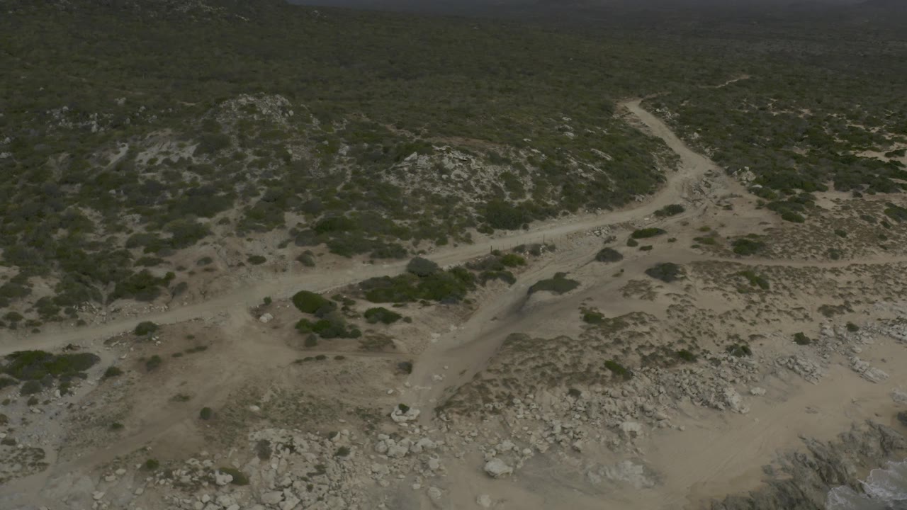 Aerial view in Baja California Sur, Mexico showing the non-paved road crossing light sandy terrain toward darker green hills, with no visible people.