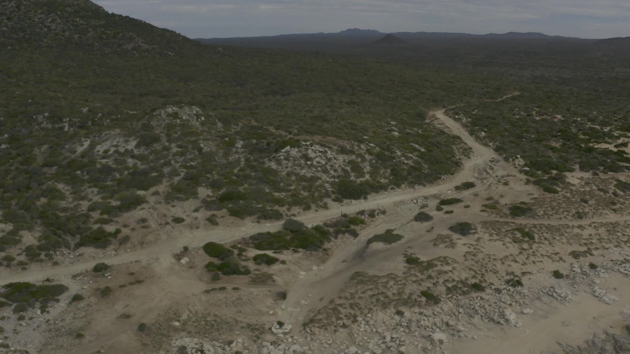 Aerial view of desert hills, green shrubs, and pale dirt tracks.