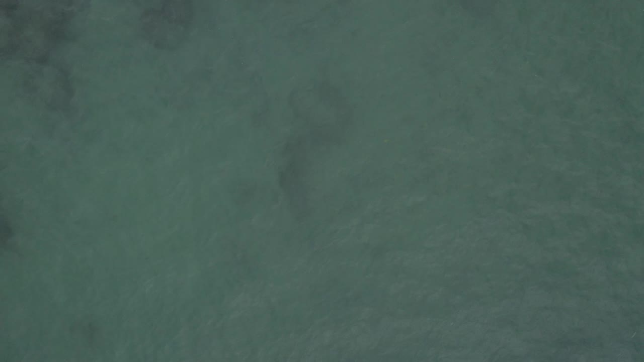 Overhead view of green-blue ocean water in Baja California Sur Mexico, with faint ripples, submerged dark patches near the upper area, and no visible people.