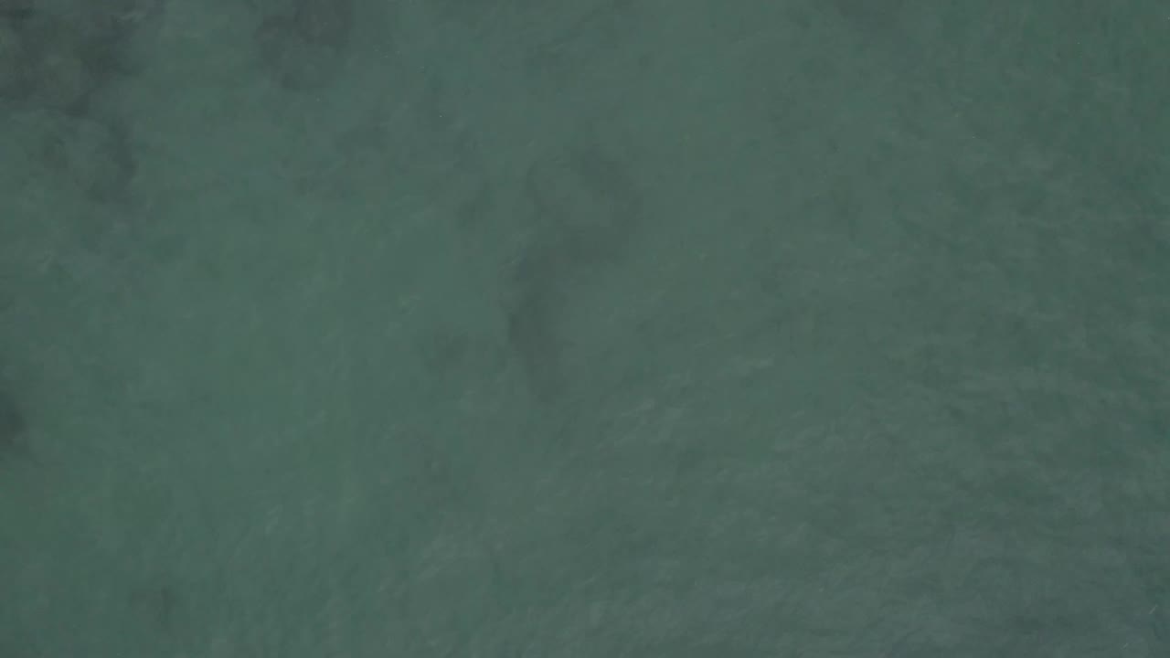 Top-down Baja California Sur ocean surface with muted teal color, soft darker shapes below the water, light surface texture, and no visible people.