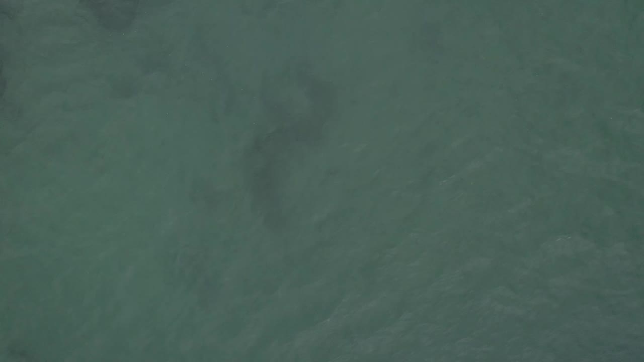 Green sea surface fills the frame, with faint ripples and uneven darker areas visible under the water in Baja California Sur, Mexico, with no visible people.