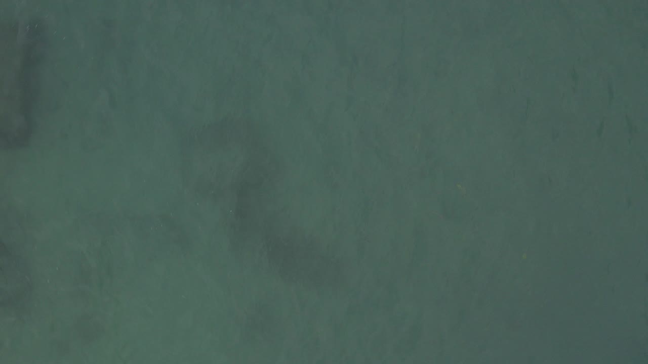 Top-down view of teal water in Baja California Sur, Mexico, with faint submerged dark streaks near the upper frame and no visible people.