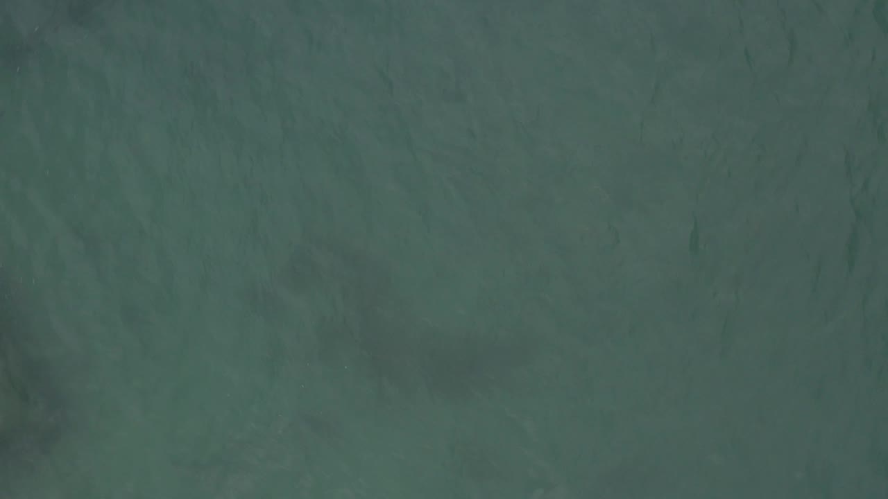 A muted teal overhead view in Baja California Sur shows a darker submerged band across the water and no visible people in the frame.