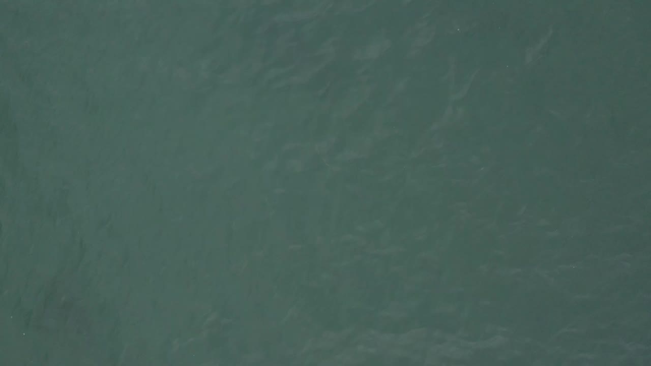 Overhead view of Baja California Sur ocean water with muted green color, light wave streaks, and no visible people.