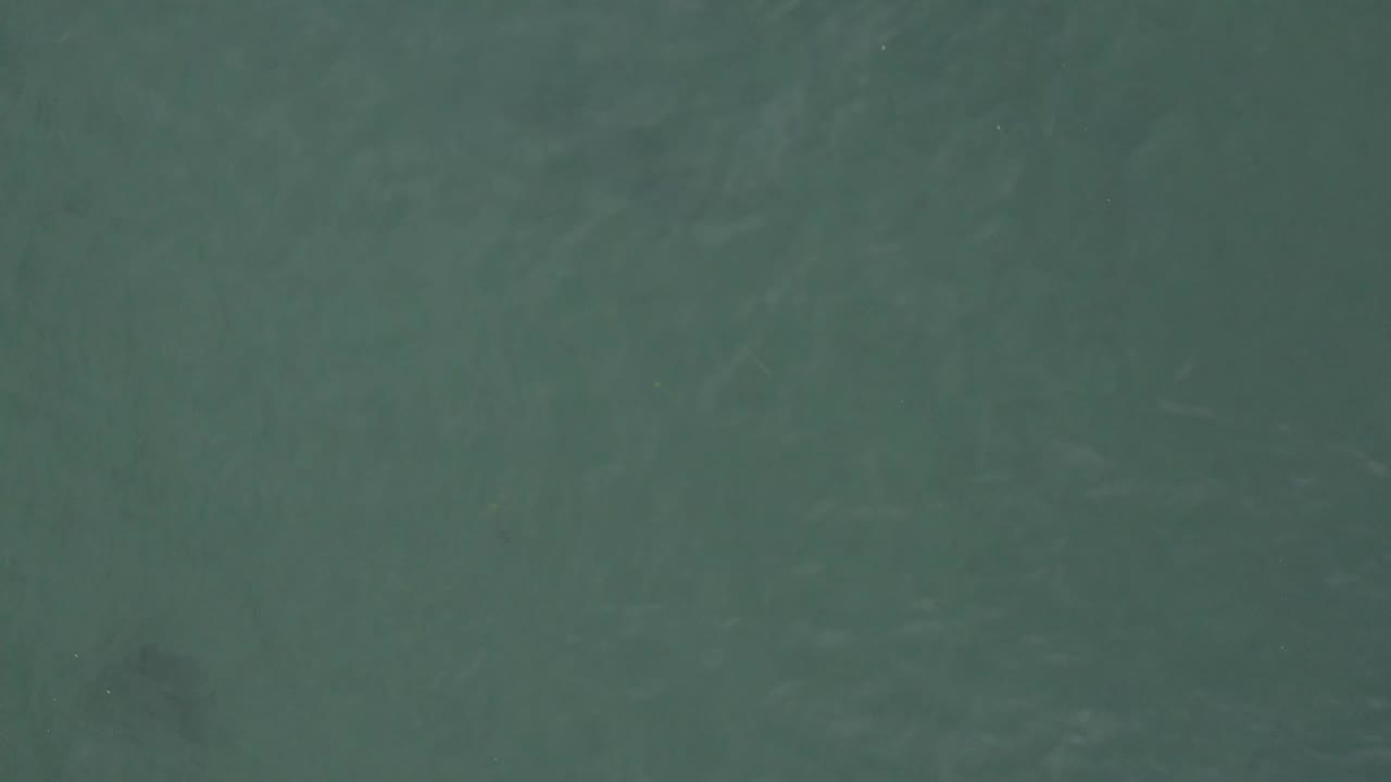 Aerial frame over Baja California Sur ocean water with soft ripples and a dark underwater shape near the upper-left area, no visible people.