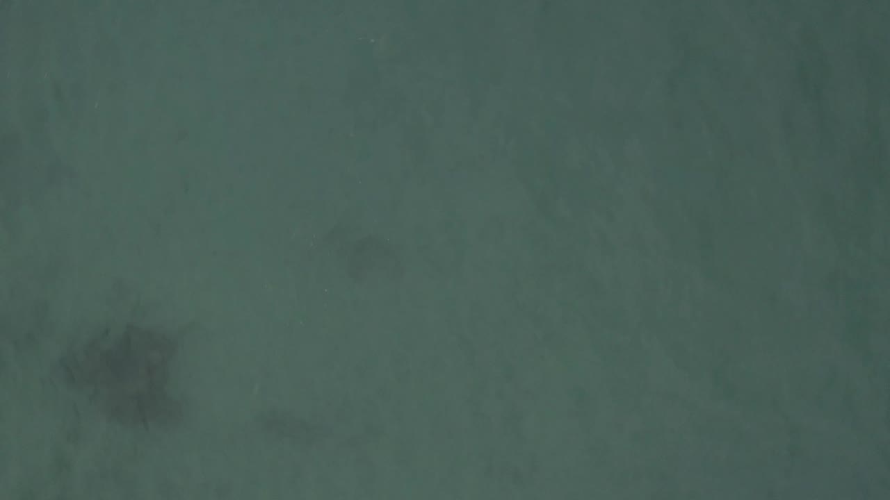 Aerial frame from Baja California Sur, Mexico, with a soft gray underwater shape set against open green-blue water and no visible people.