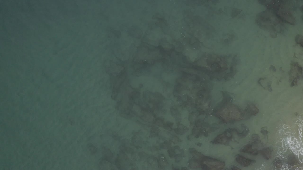 Overhead shallow green-blue water with dark submerged rocks and pale sand.