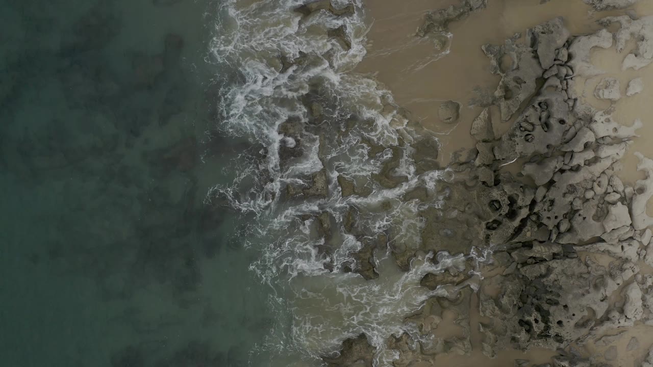 Foam spreading across dark shoreline rocks