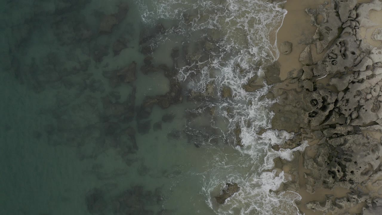 Overhead surf breaking beside rocks and sand