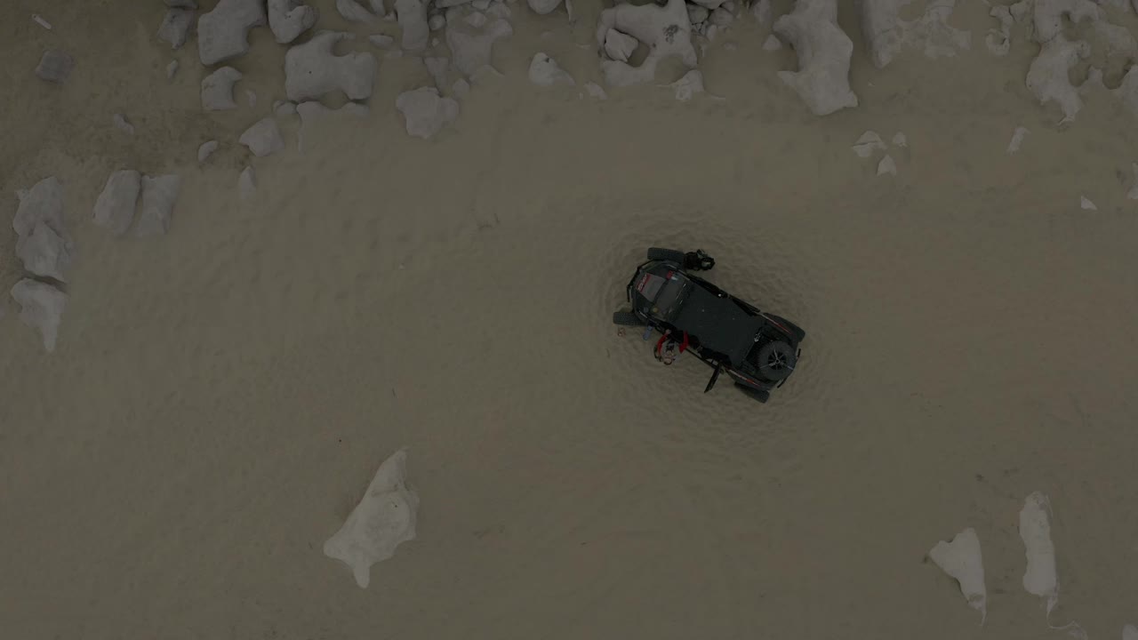 Aerial view from Baja California Sur, Mexico with a black vehicle positioned on open sand beneath scattered rock shapes, with no visible people discernible.