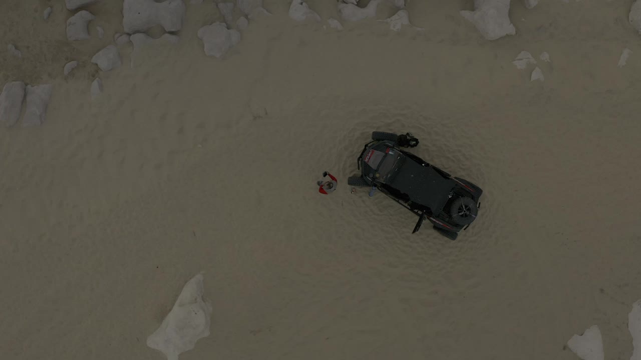 Aerial frame from Baja California Sur, Mexico, showing the vehicle shifted toward the right side of the sandy frame with light rocks at the edges and no recognizable faces.