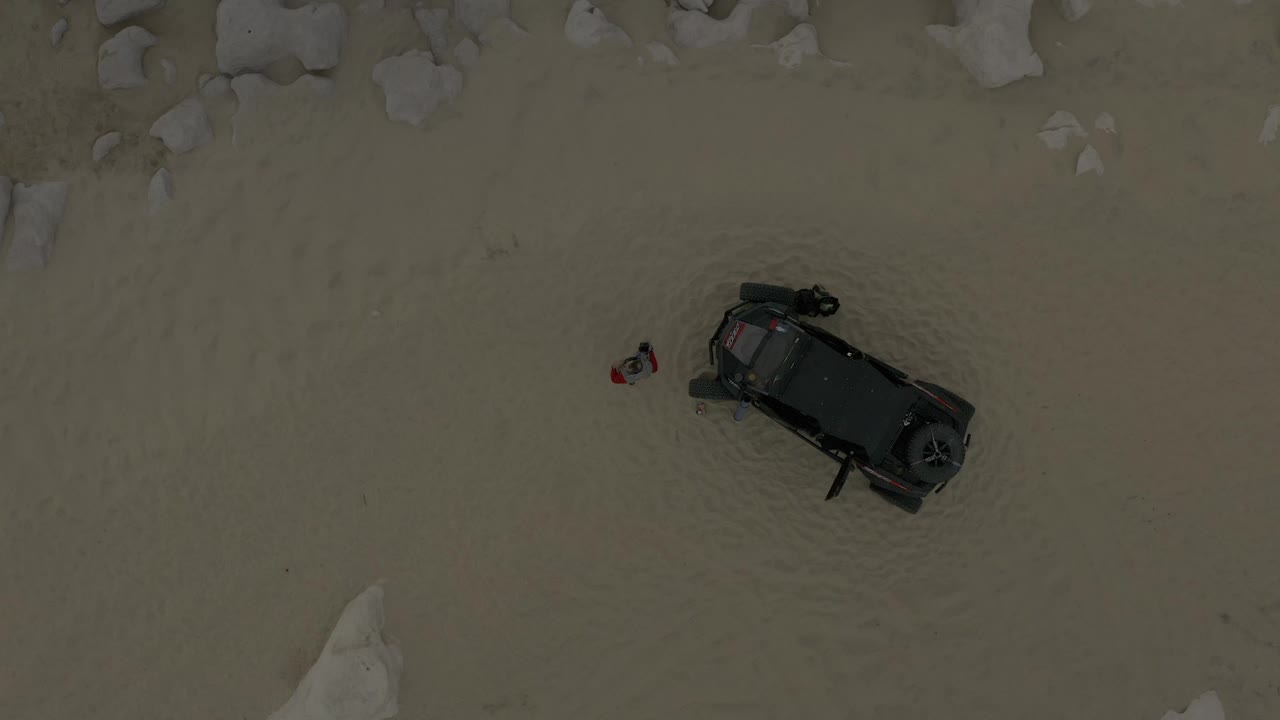 Top-down Baja California Sur frame with the dark vehicle near midframe, pale rock formations at the upper and lower edges, and no recognizable people visible.