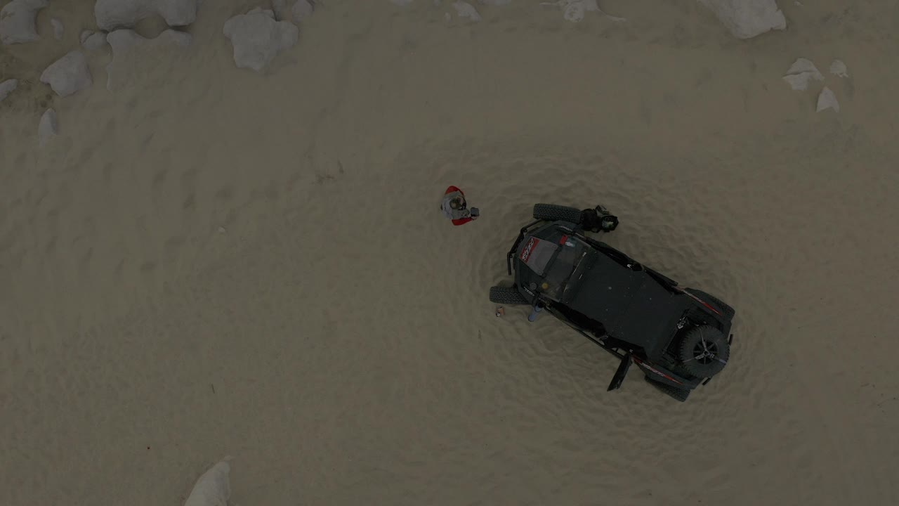 Overhead frame in Baja California Sur Mexico showing a small child in a red shirt standing on pale sand above a dark off-road vehicle.