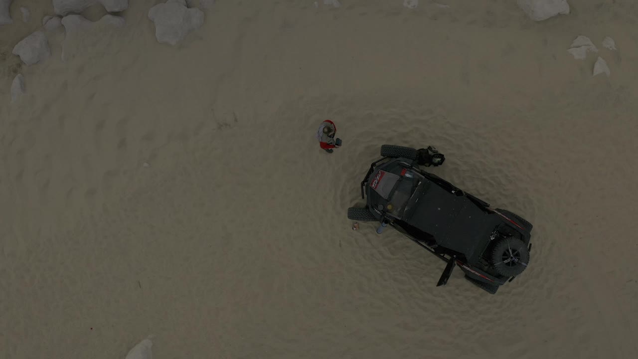 Aerial frame in Baja California Sur Mexico showing the child in red near the upper left of a dark off-road vehicle on open sandy terrain.