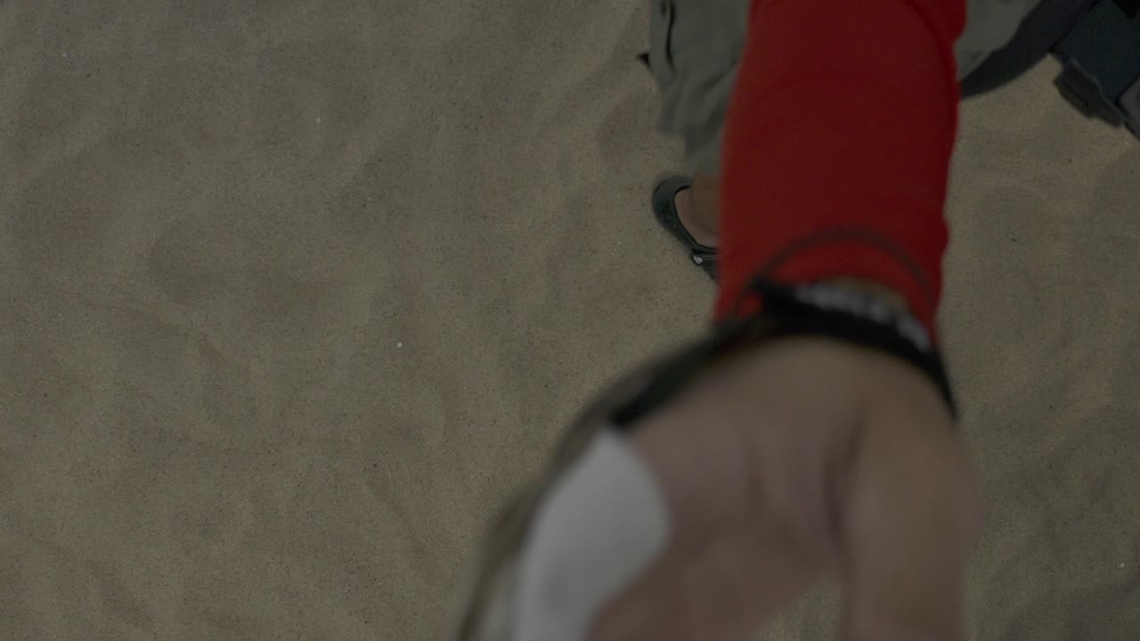 Close foreground view in Baja California Sur, Mexico, with a red-sleeved arm and hand over tan beach sand, with no visible face in this frame.