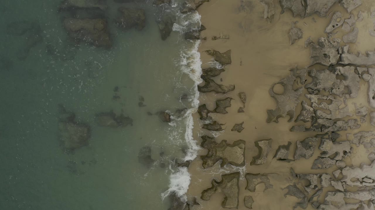 Overhead surf line beside rocks and sand