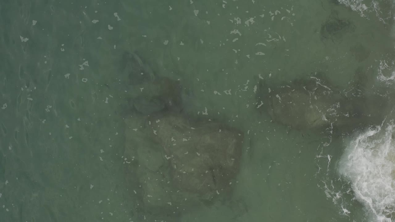 Overhead sea surface with underwater rock shapes and a foam burst near the lower right.