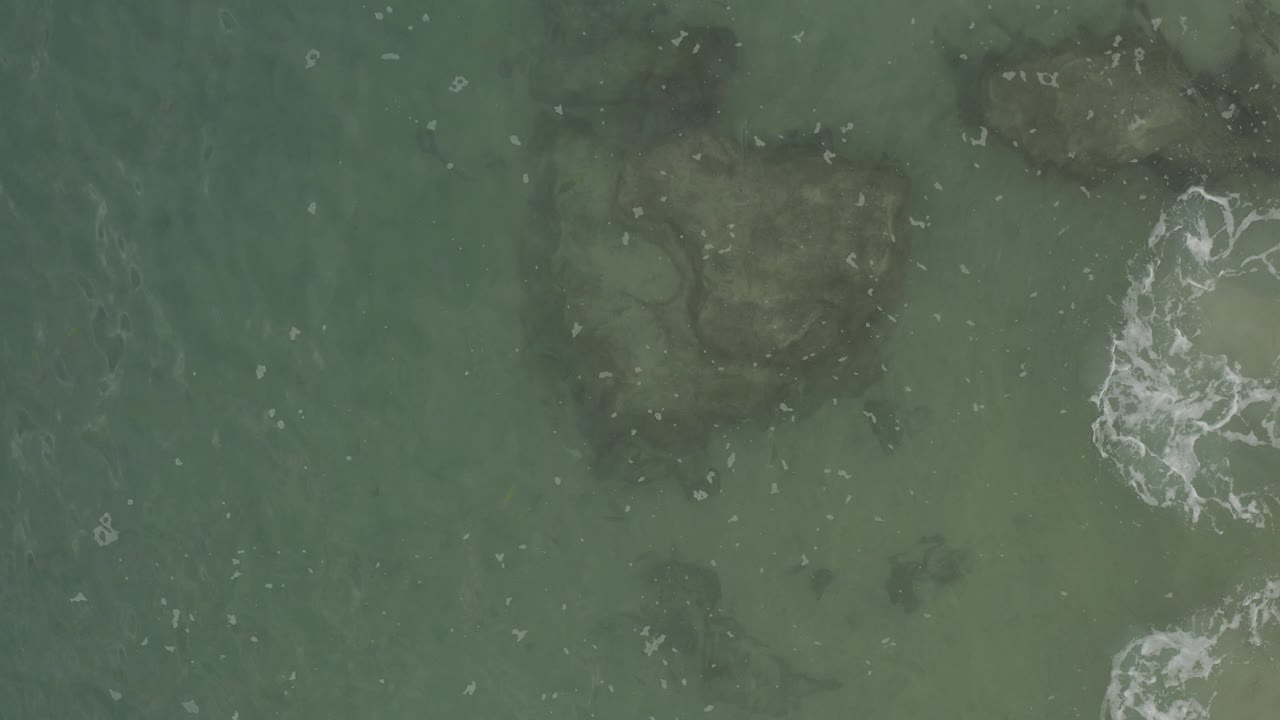 Overhead green ocean water with submerged rocks and white foam.
