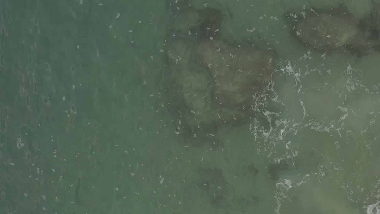 Clear shallow ocean surface with ripples over darker underwater shapes.
