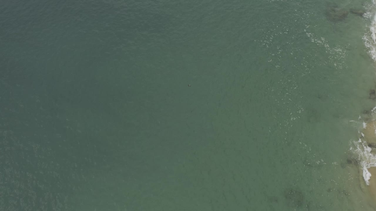 Overhead Baja California Sur coastal water with a light reef or sand patch under the surface and a small area of white foam near the right side.