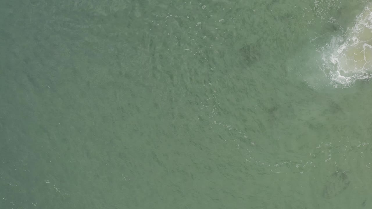 Aerial view over Baja California Sur ocean water, with white foam gathered around a pale submerged area near the top right and no visible people.