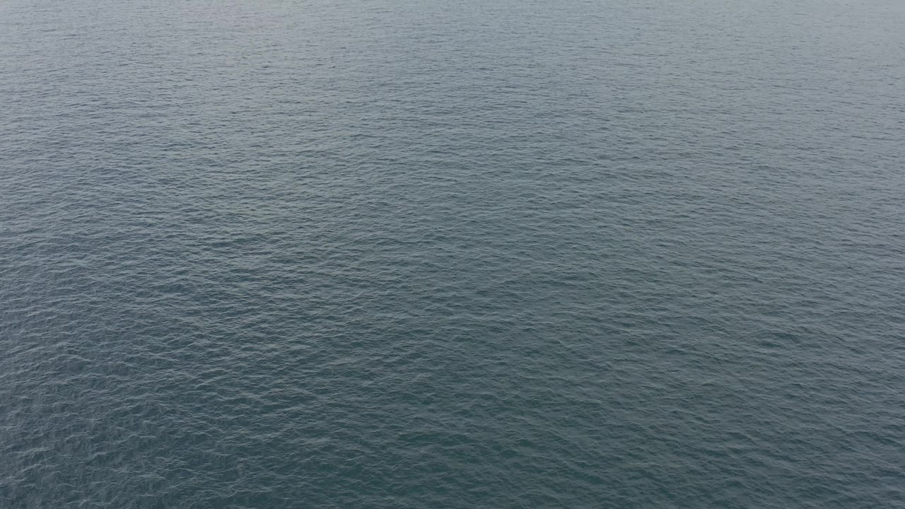 A calm blue-green water surface continues across the Baja California Sur frame under hazy daylight, with no visible people or structures.