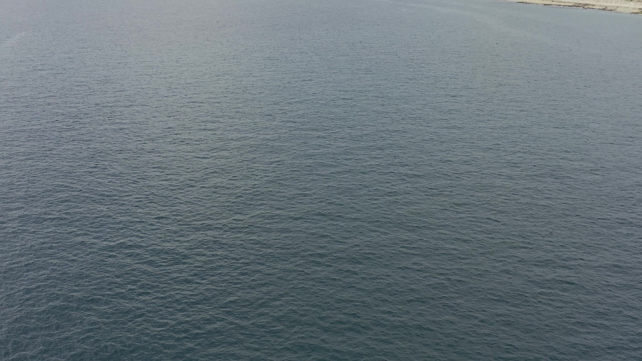 Aerial frame from Baja California Sur, Mexico showing rippled blue-green water filling most of the view, a thin tan beach at the top edge, and no visible people.