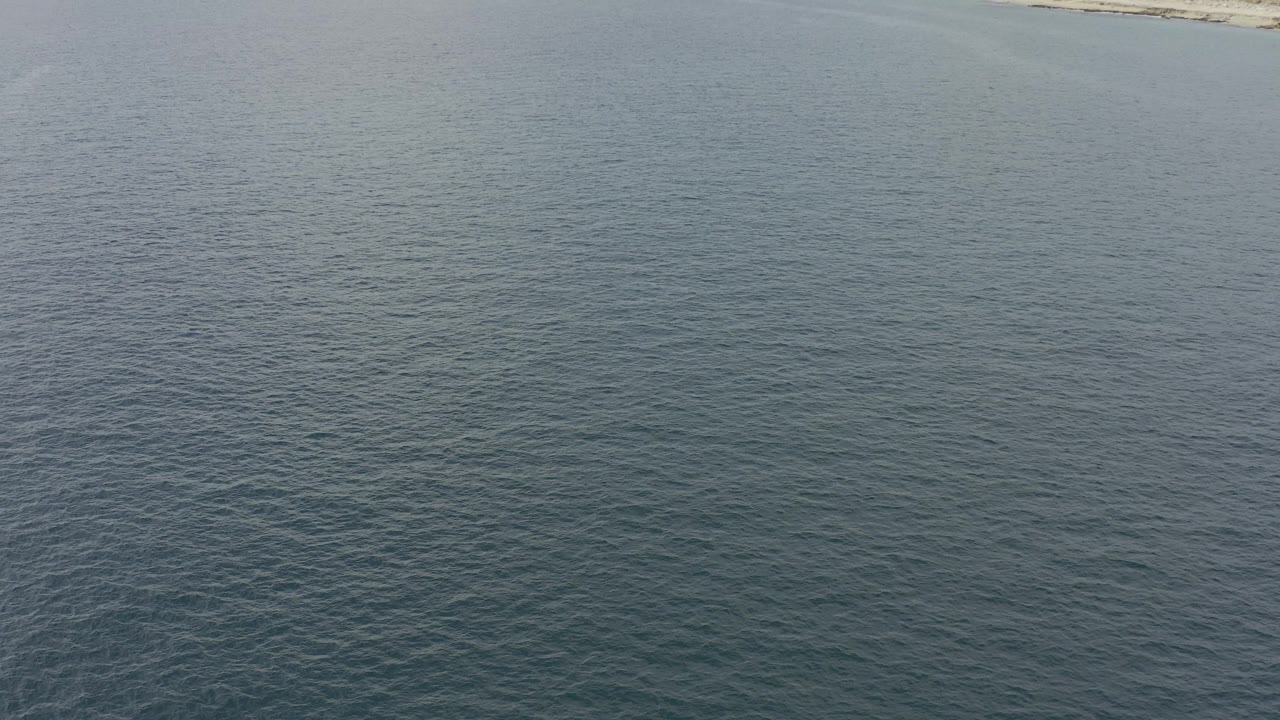 Aerial frame from Baja California Sur, Mexico with textured calm water across the foreground and a pale beach barely visible along the upper border, with no visible people.