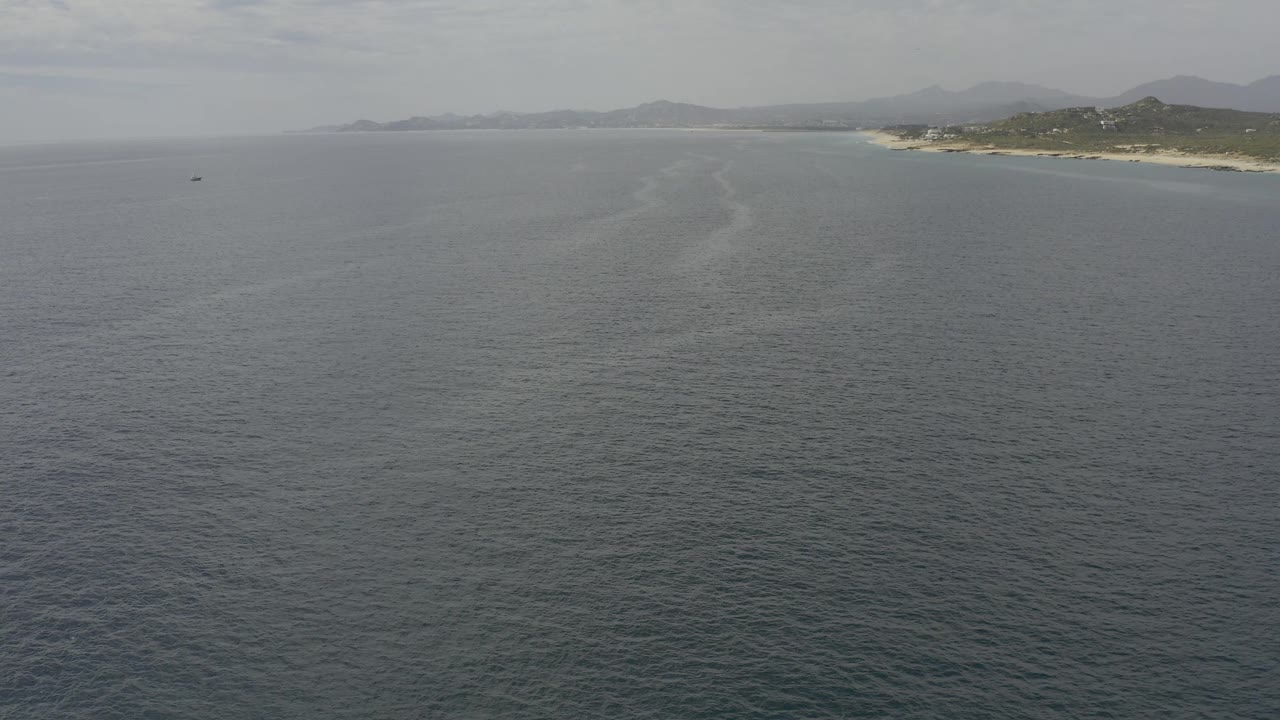 Second frame of the Baja California Sur aerial shows the small dark boat left of center, textured open water below, and the coastline running across the upper right with no visible people.