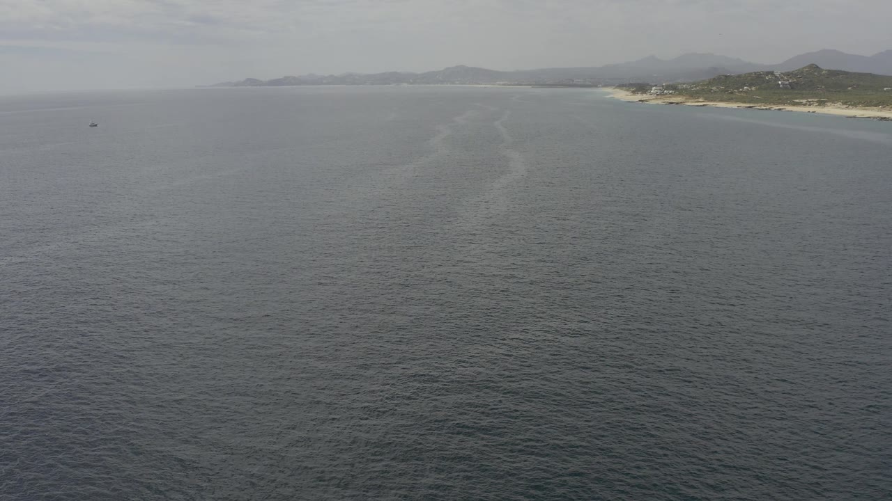 Aerial view in Baja California Sur with textured ocean across the foreground, pale disturbed water near center, and coast and hills along the upper right, no visible people.