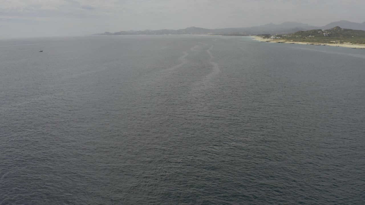 Baja California Sur coastline seen from above, with blue gray ocean dominating the frame and a light streak of water pointing toward the beach, no visible people.