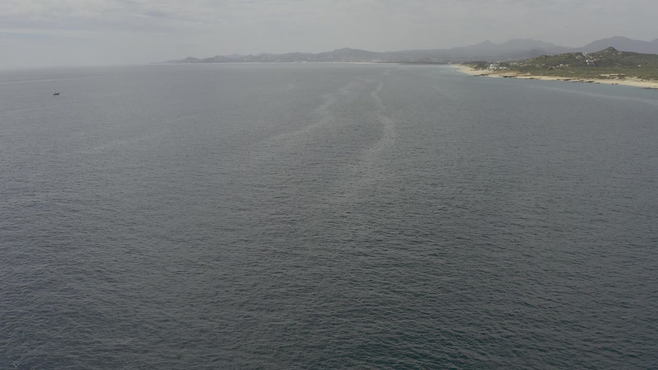 Aerial view over Baja California Sur water with a sandy coastline and low hills along the right horizon, no visible people.