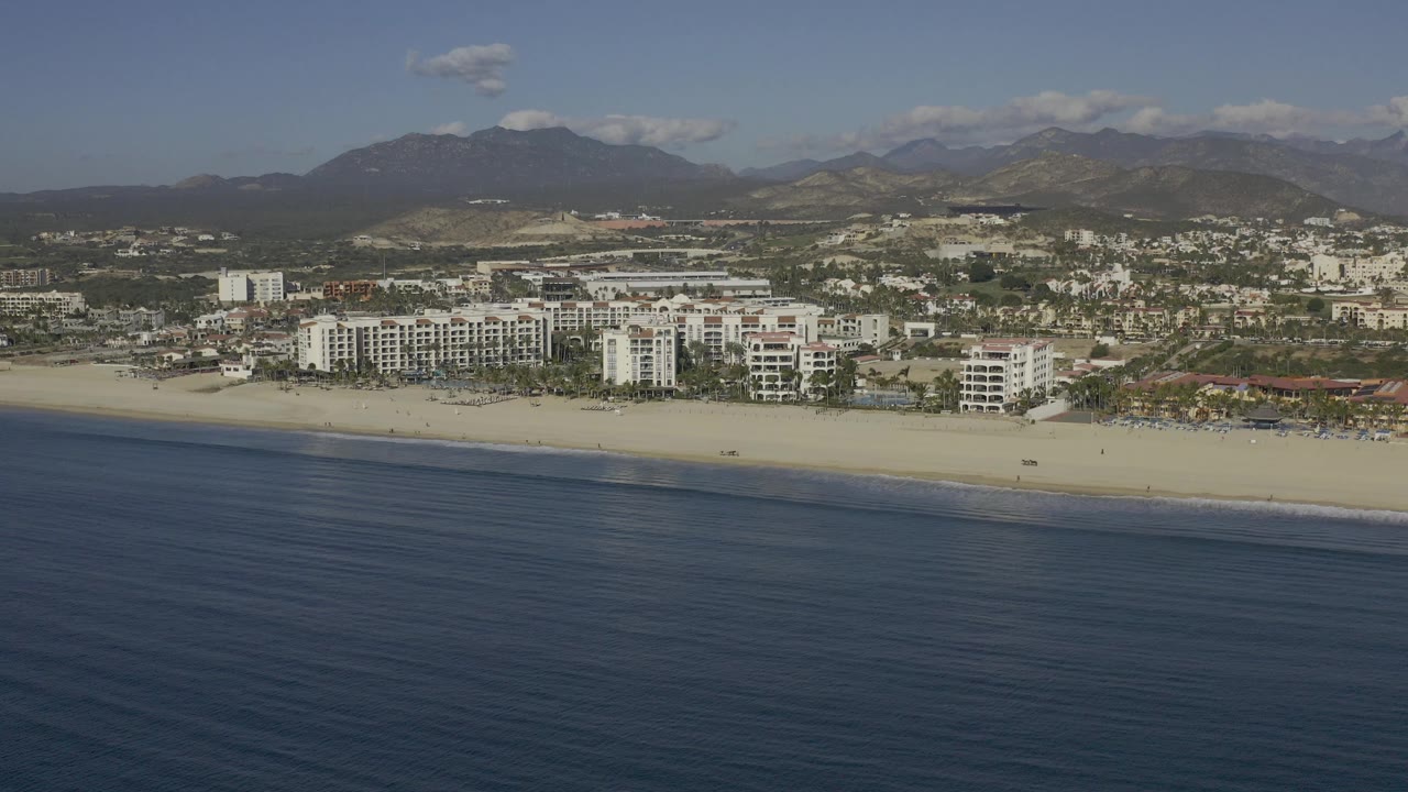 Aerial view of ocean, beach, beachfront buildings, town, and mountains.