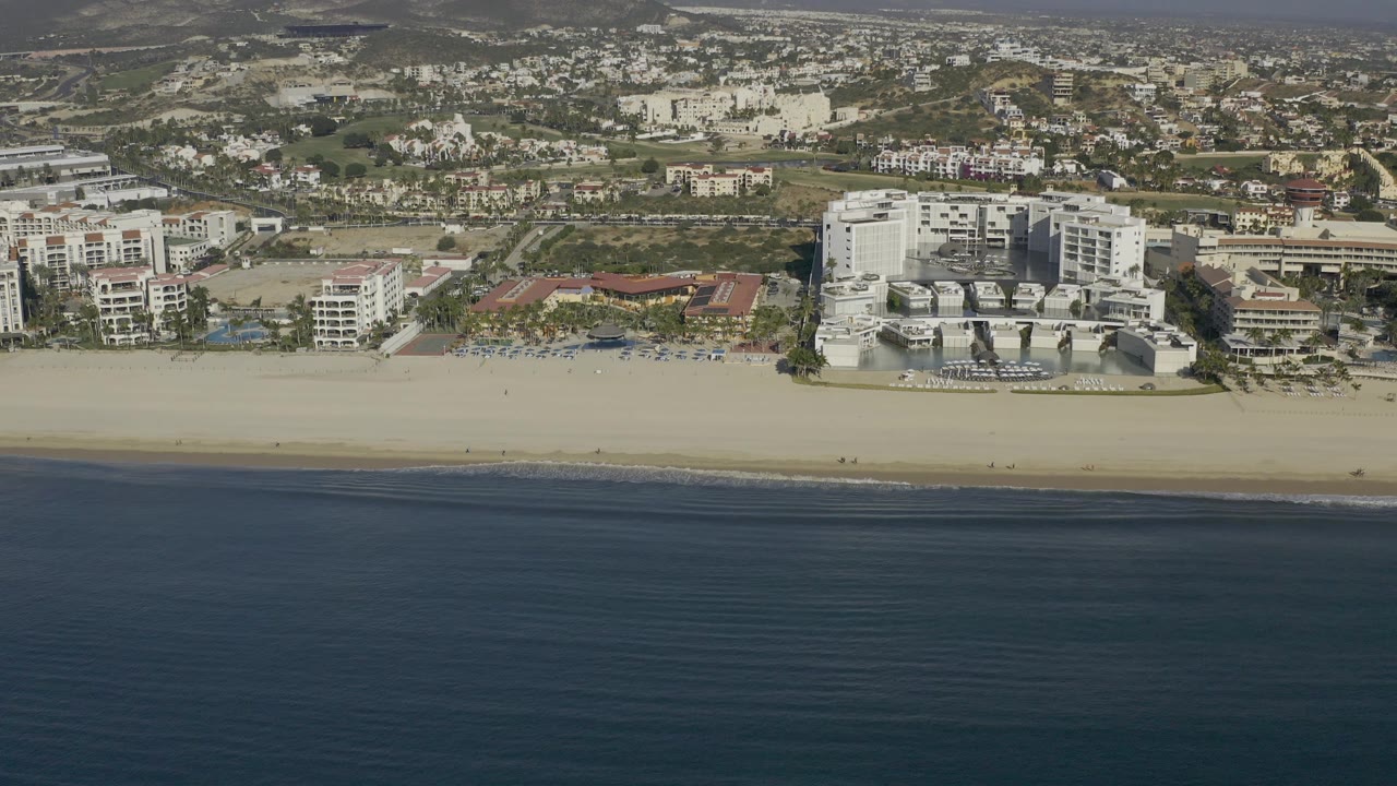 Aerial shoreline view with beach, hotels, pools, and inland neighborhood.