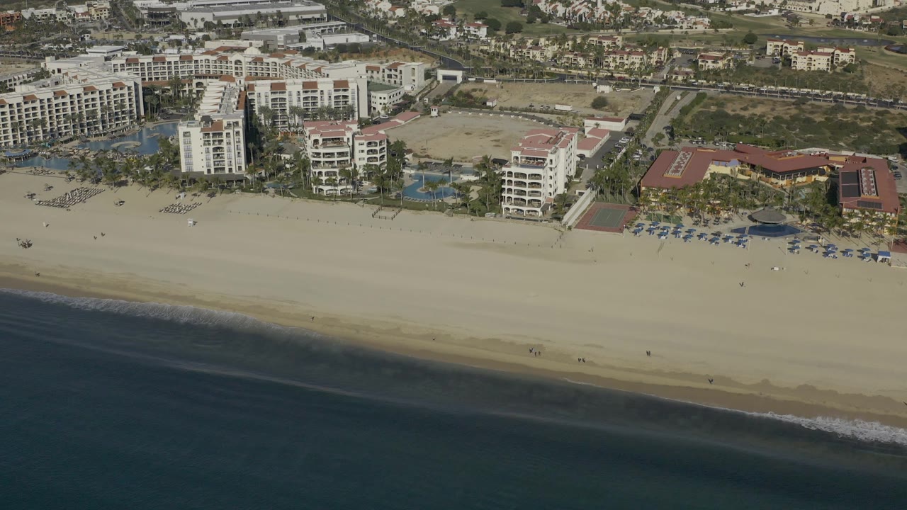 Aerial shoreline view with hotels, beach umbrellas, and surf.