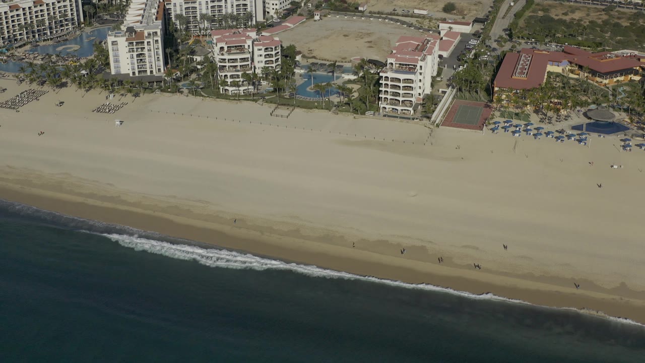 Aerial view of foamy waves reaching the sandy beach below coastal hotels.