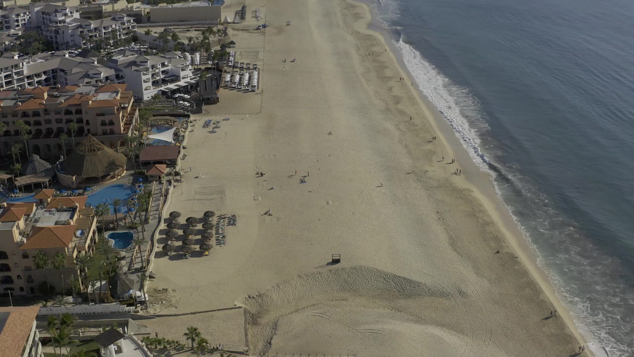 A second overhead frame in Baja California Sur shows the same beachfront from a slightly shifted position, with more open sand visible between the buildings and the surf.