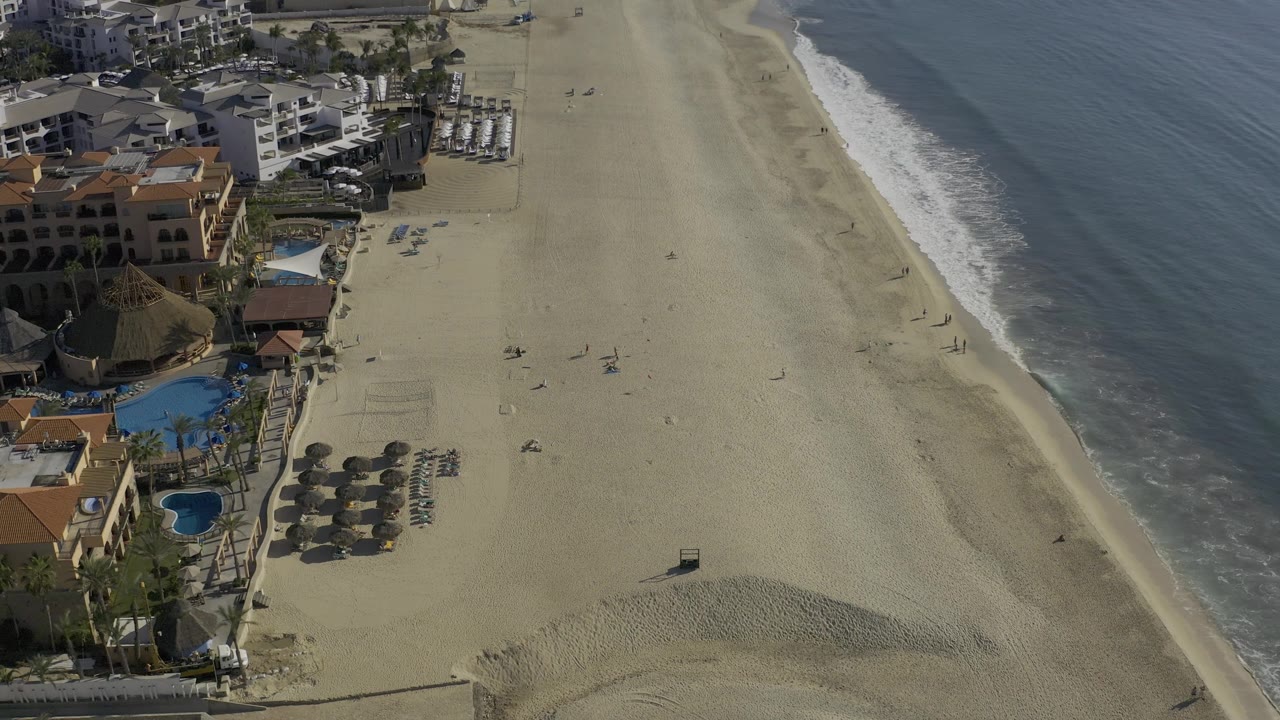 Overhead beach view with buildings, pools, and ocean.