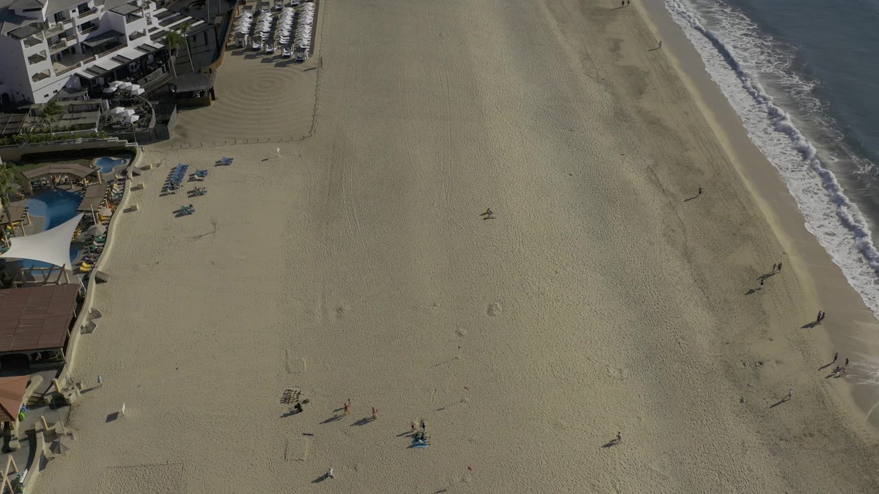 Drone view of resort chairs and open sand beside the waterline.