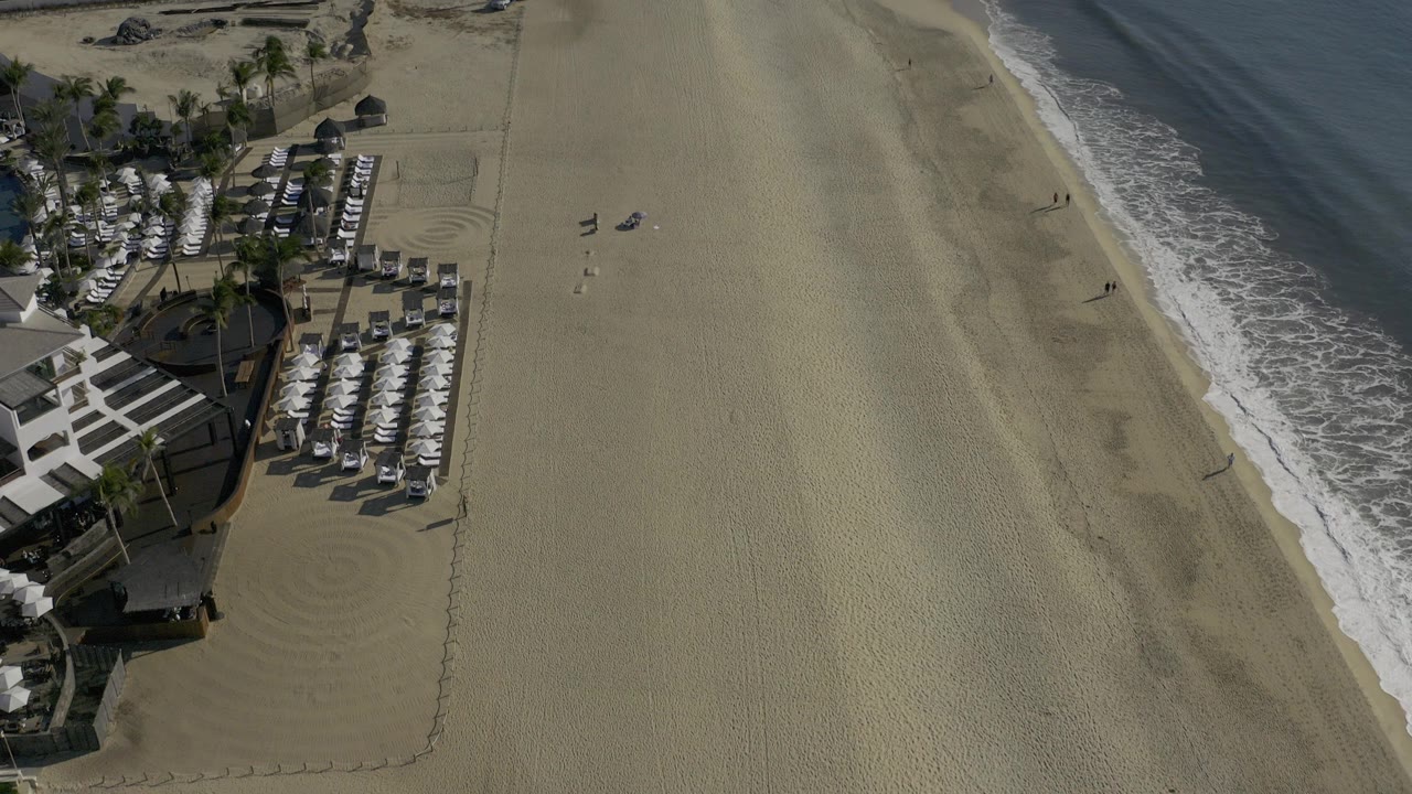 High aerial view of tan beach, surf, umbrellas, and blue water.