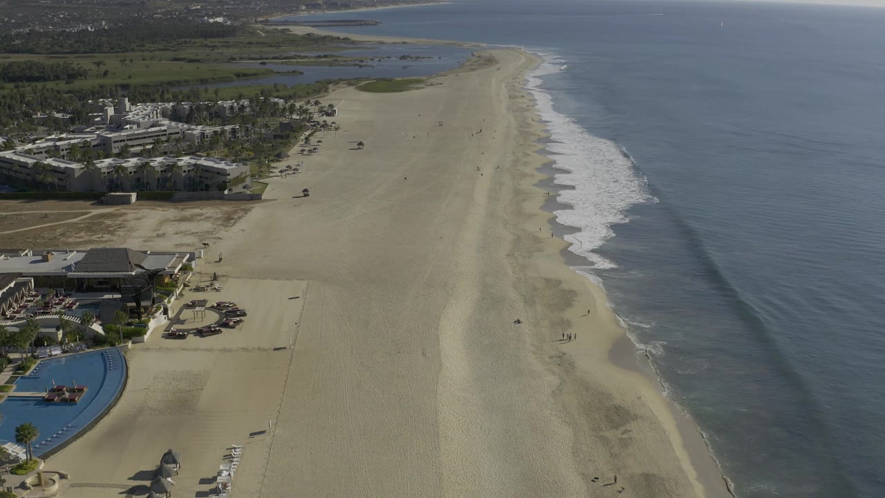 Aerial beach view with resort pool corner, open sand, and gentle surf.
