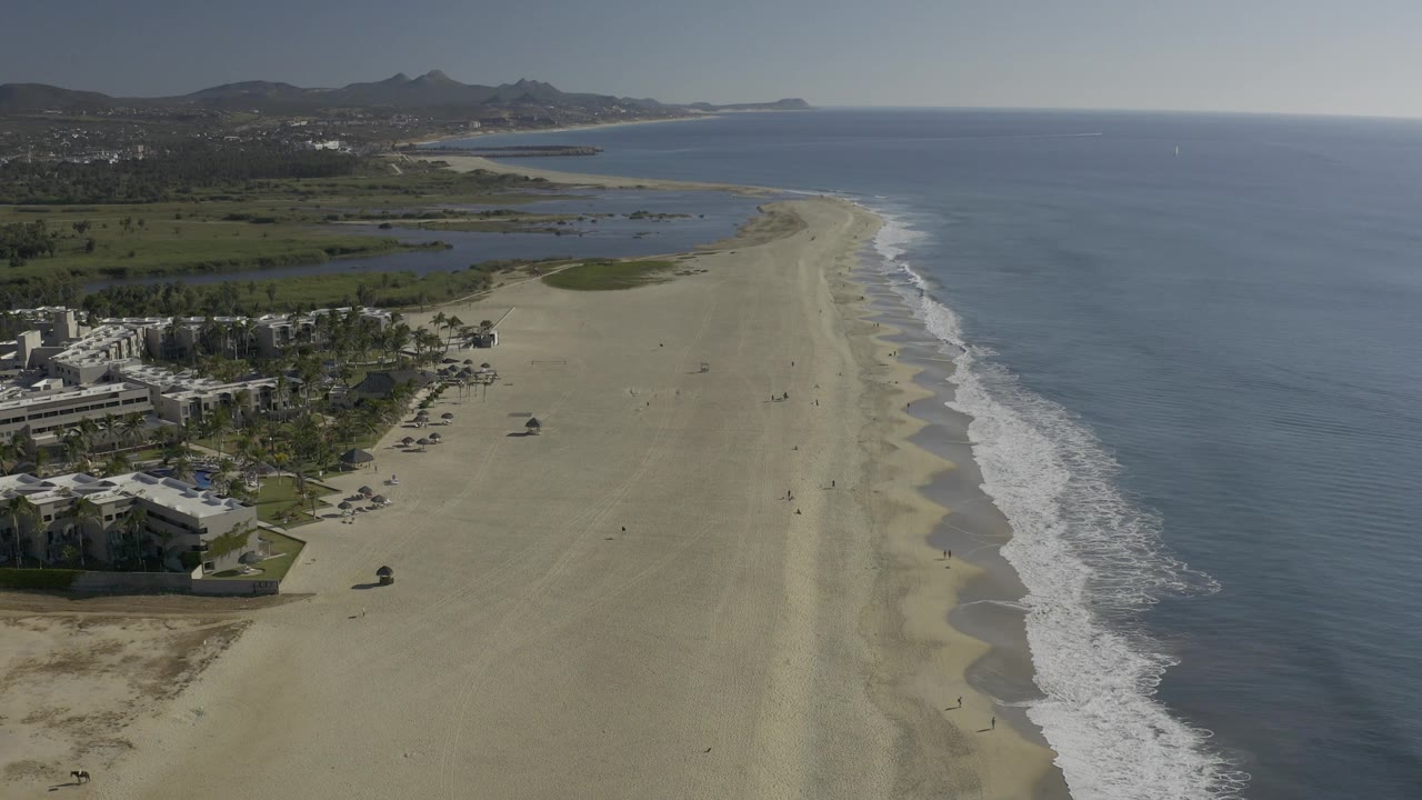 Aerial coastline with surf running along a broad sand beach.