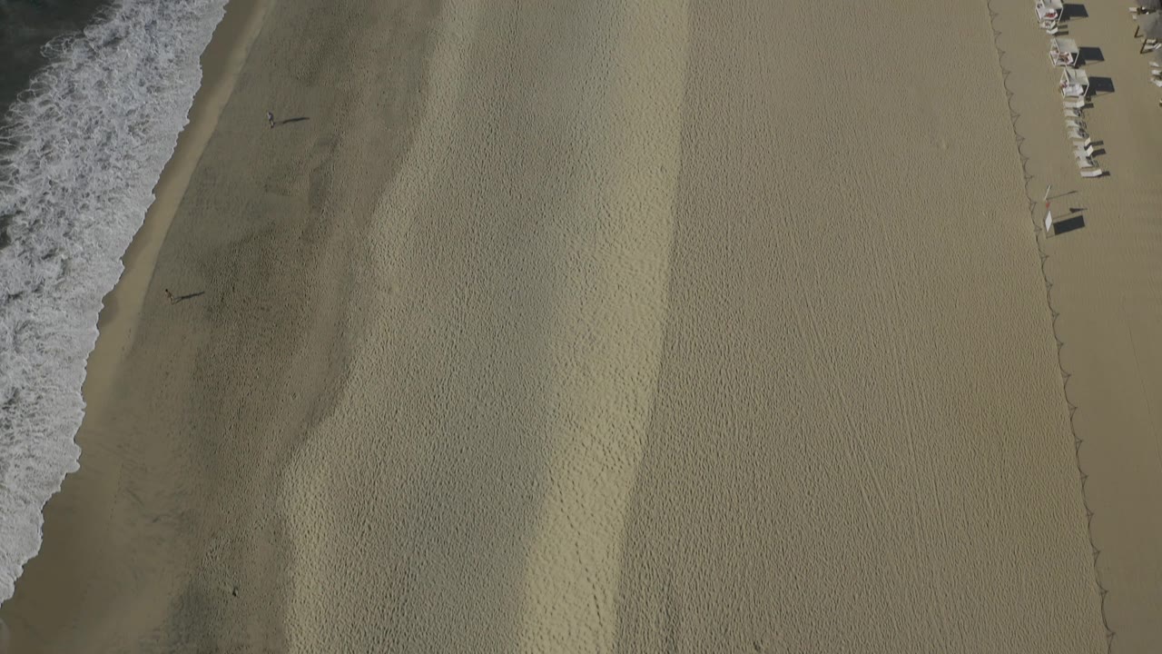 Drone view of surf, wet sand, dry sand, and beach loungers.