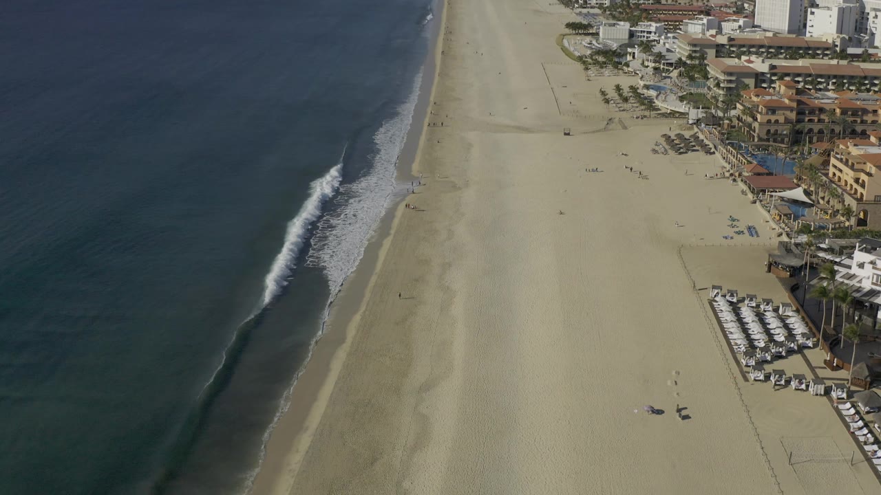 High coastal view with waves, open sand, and hotels along the beach edge.