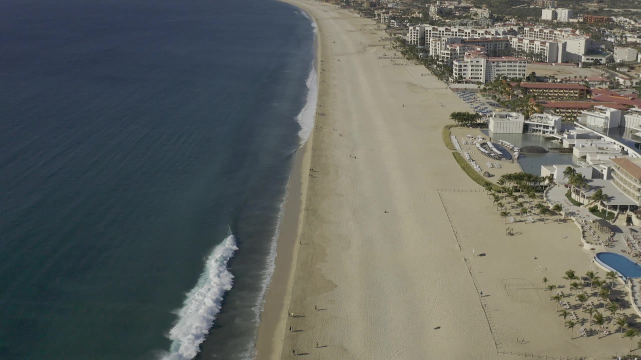 Aerial view of surf rolling onto sand beside beachfront development.