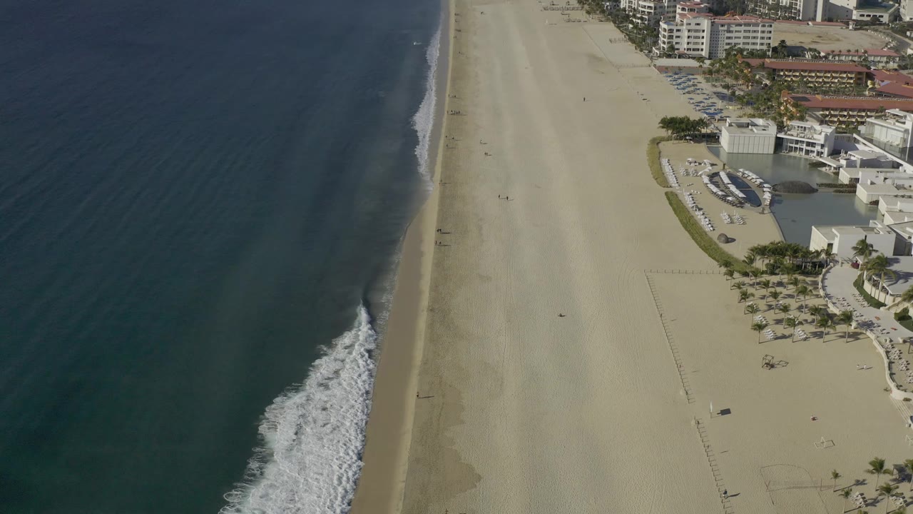Overhead coastline with surf line, open beach, and buildings beside the sand.