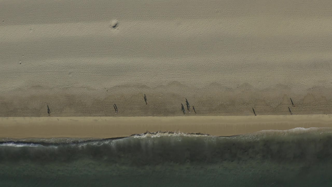 Top-down Baja California Sur beach view with small walkers above the foam line and smooth sand filling most of the frame.