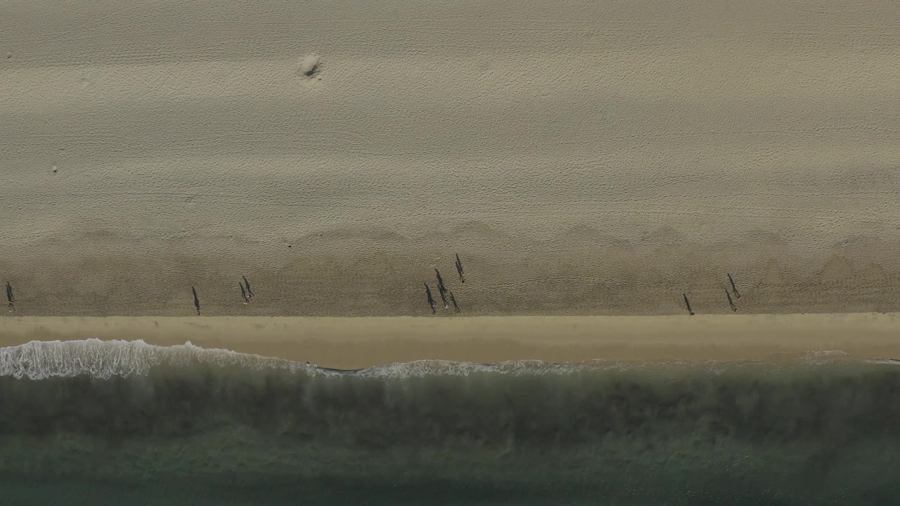 Aerial beach frame with walkers spaced along the waterline.