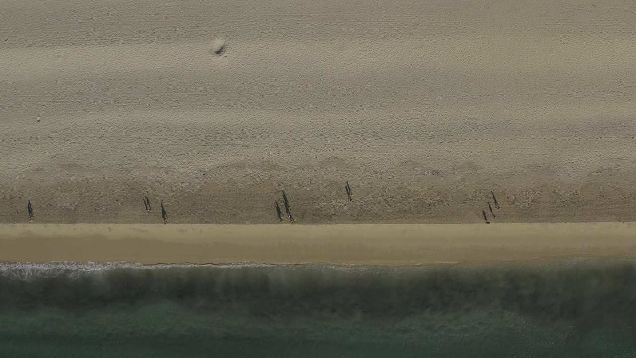 Straight-down beach view with walkers casting shadows