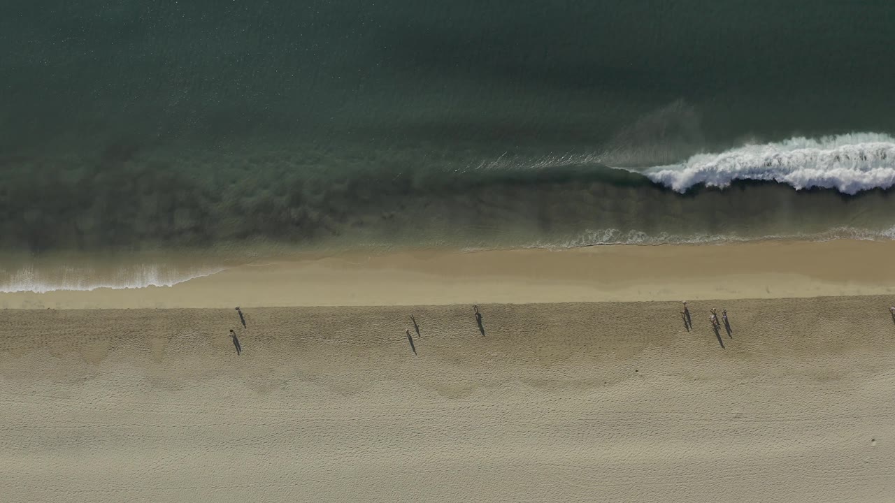 Overhead beach scene with a foamy wave spreading along the shoreline.